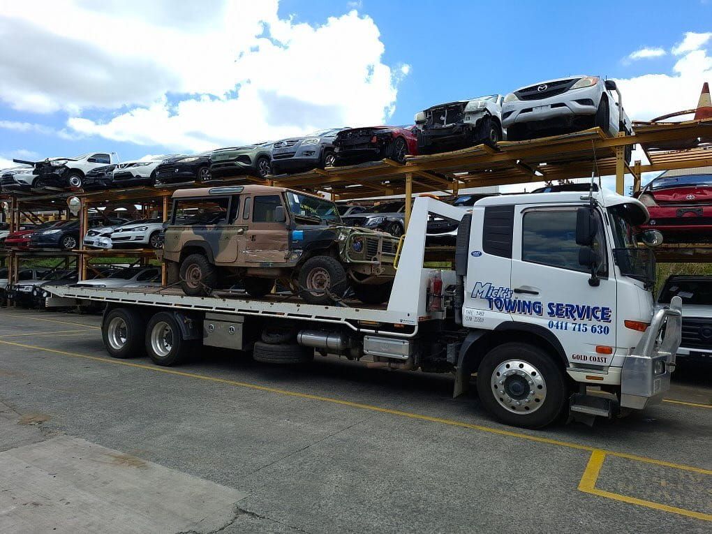 A Tow Truck Carrying a Bunch of Cars is Parked in a Parking Lot — Mick's Towing Service Pty Ltd in Carrara, QLD