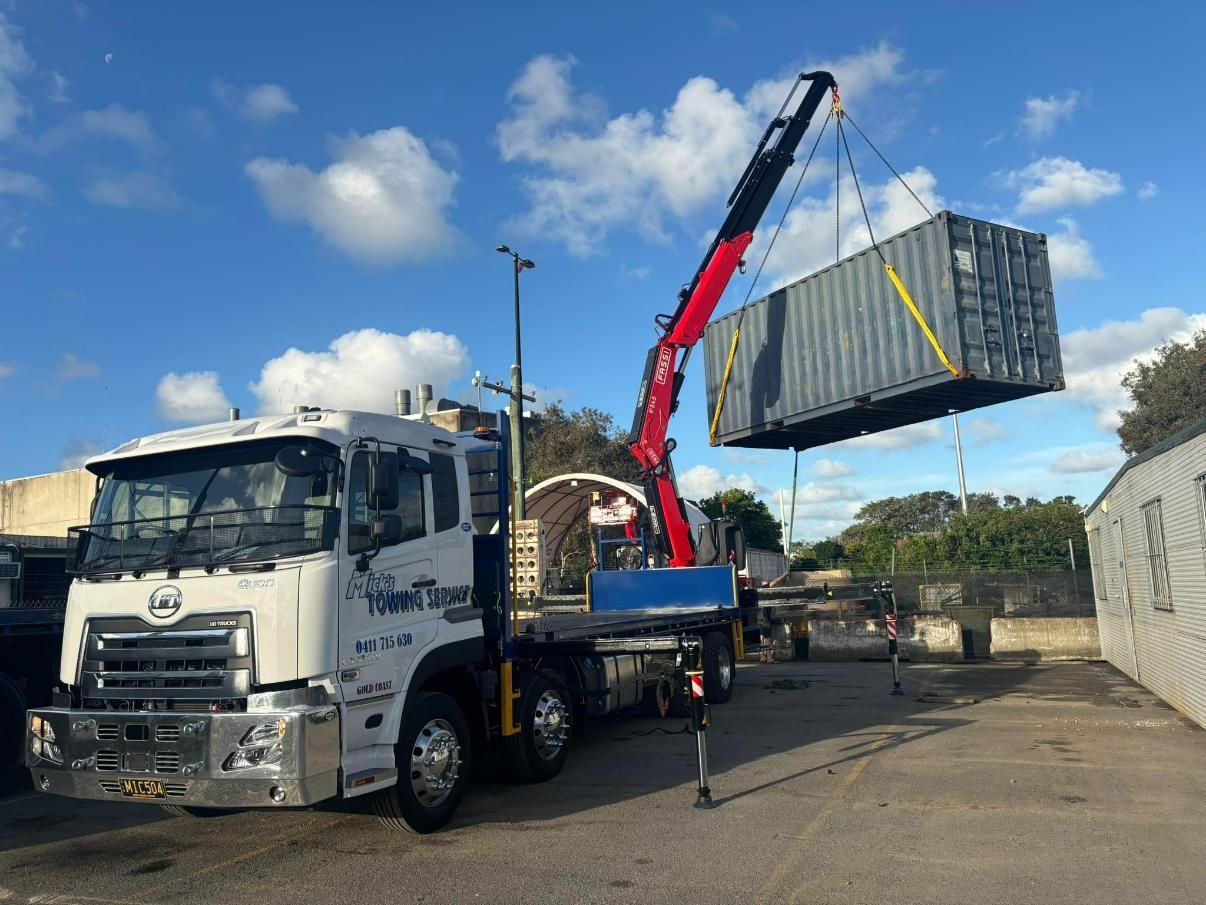 A Truck With a Crane Attached to It is Lifting a Container — Mick's Towing Service Pty Ltd in Carrara, QLD