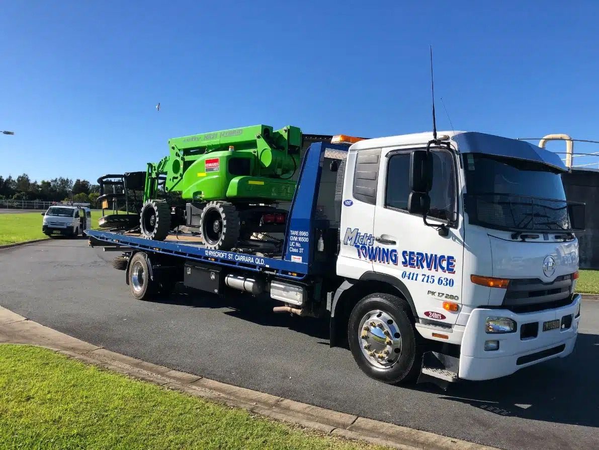 A Tow Truck is Carrying a Green Machine on the Back of It — Mick's Towing Service Pty Ltd in Carrara, QLD