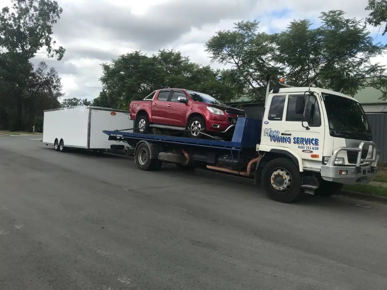 A Tow Truck is Towing a Trailer With Two Cars on It — Mick's Towing Service Pty Ltd in Carrara, QLD