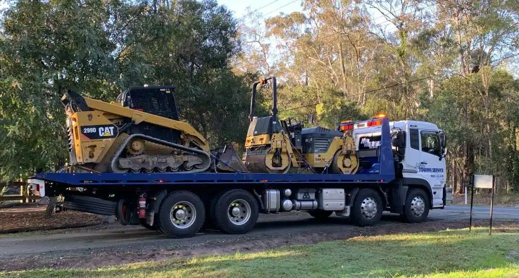 A Tow Truck is Carrying a Bulldozer on the Back of It — Mick's Towing Service Pty Ltd in Carrara, QLD