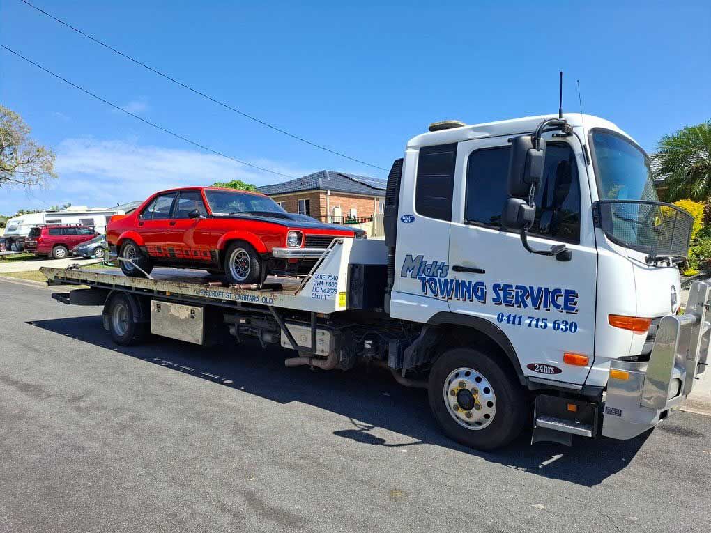 A Tow Truck With a Red Car on the Back — Mick’s Towing Service Pty Ltd in Carrara, QLD
