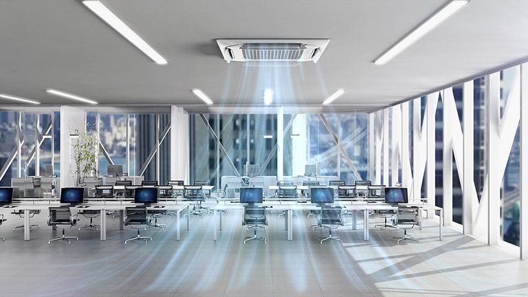 An office with an overhead air conditioning unit blowing cool air, computers, and desks.