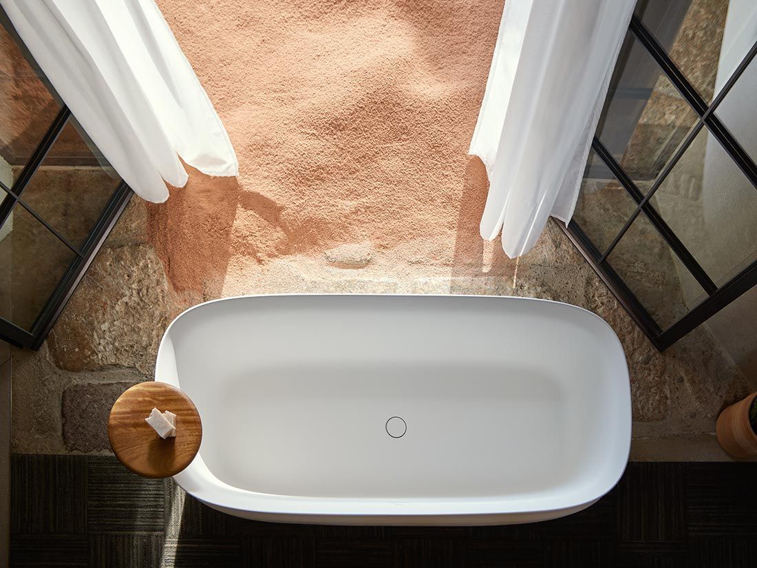 Baignoire blanche dans une salle de bains rustique aux murs de pierre et aux rideaux transparents.