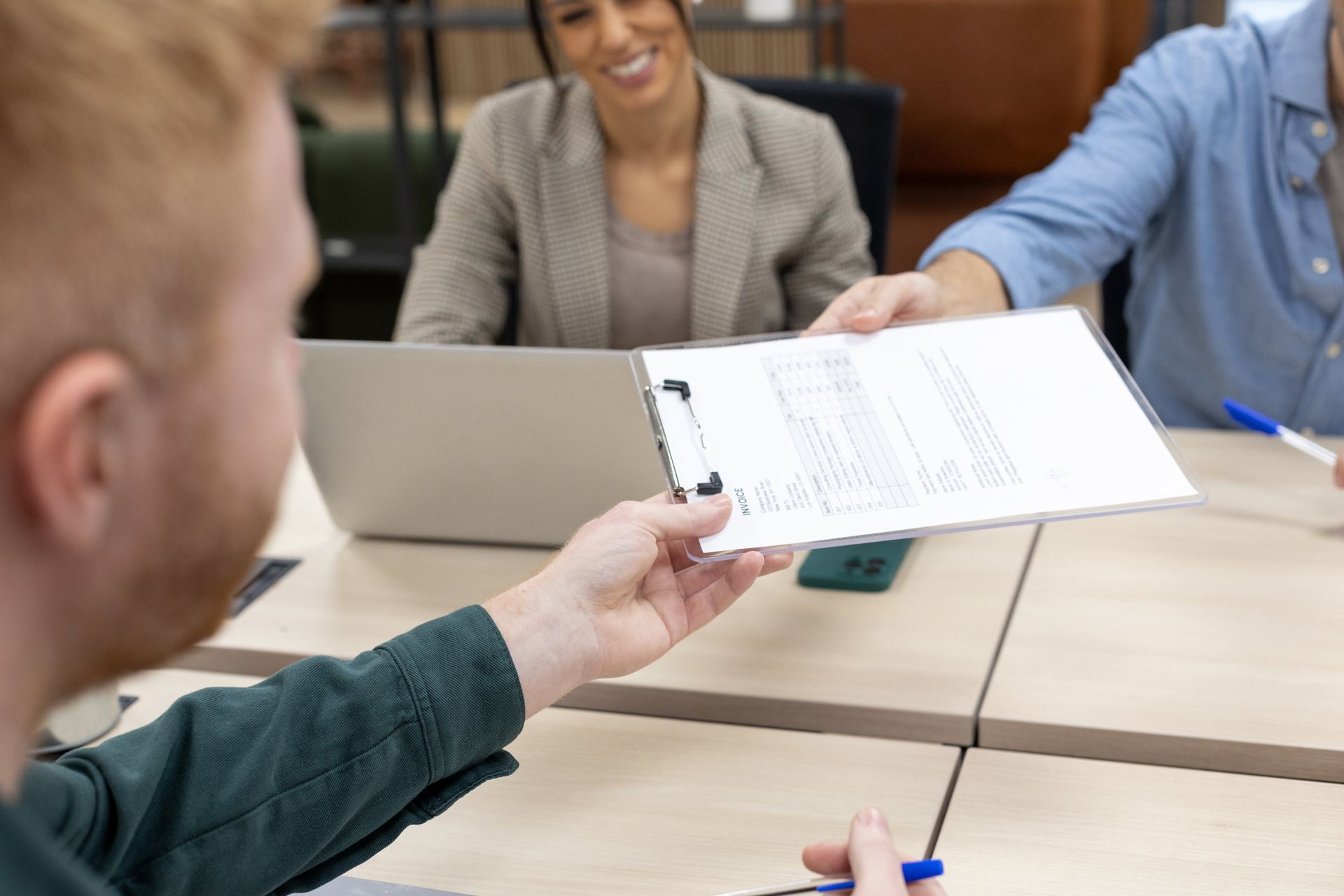 Dans un bureau, une personne tend un porte-documents à une autre ; deux autres personnes sont assises à une table.