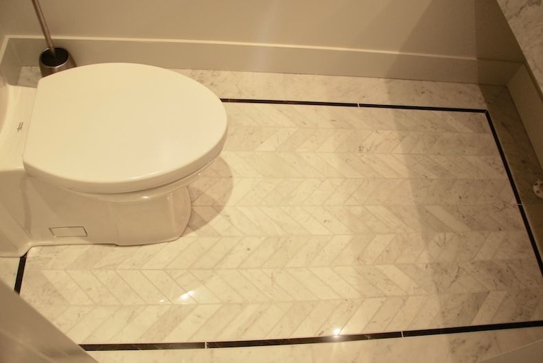 Toilettes blanches dans une salle de bains avec sol en marbre à motifs, bordé d'une bande noire.