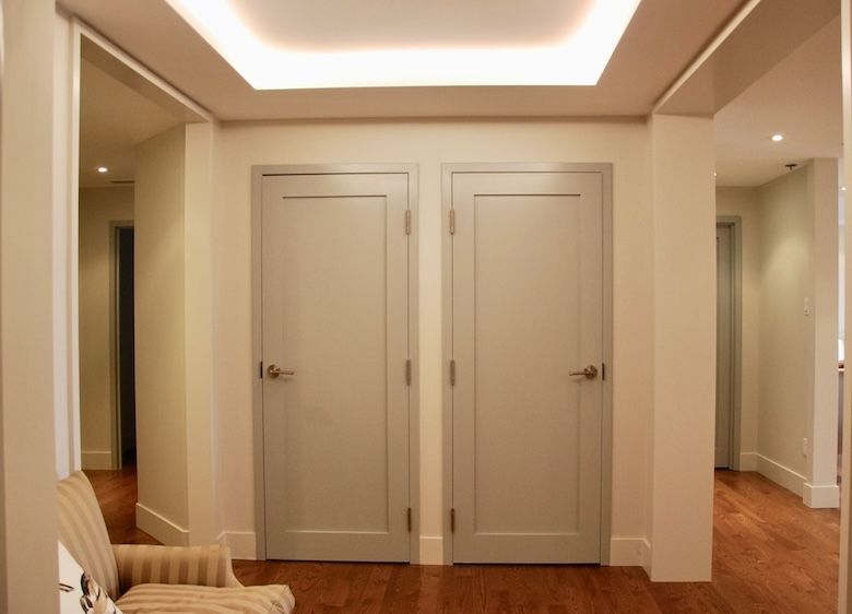 Deux portes grises dans un couloir. Murs beiges, parquet et plafonnier encastré.