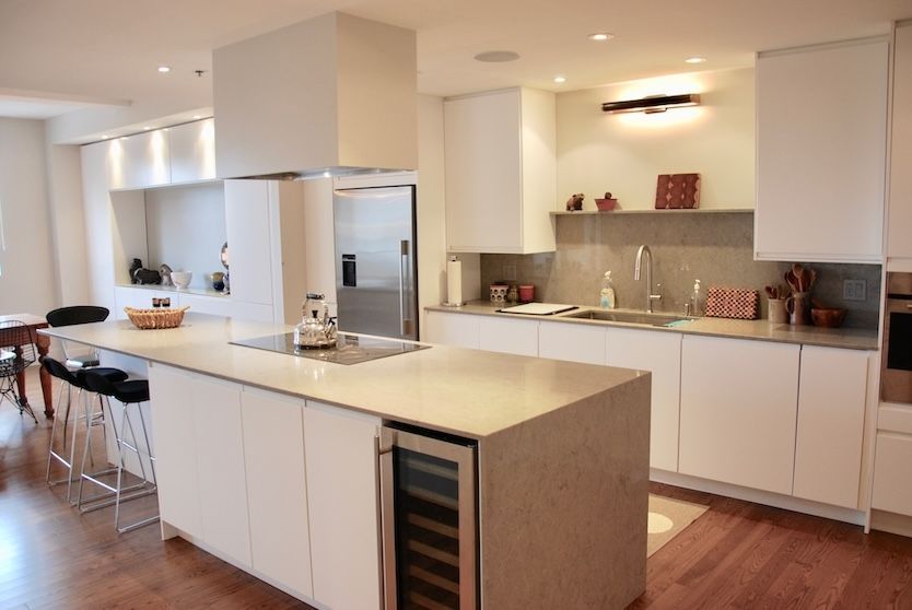 Cuisine moderne blanche avec îlot central, électroménagers en acier inoxydable et planchers de bois franc.