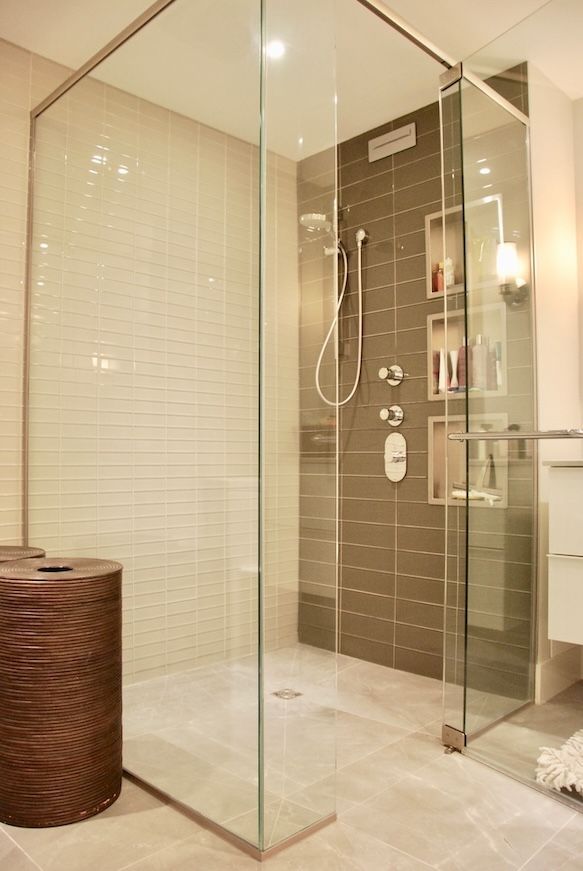 Douche vitrée dans une salle de bains moderne. Mur d'accent carrelé de brun avec étagères, sol gris clair et tabouret en bois.