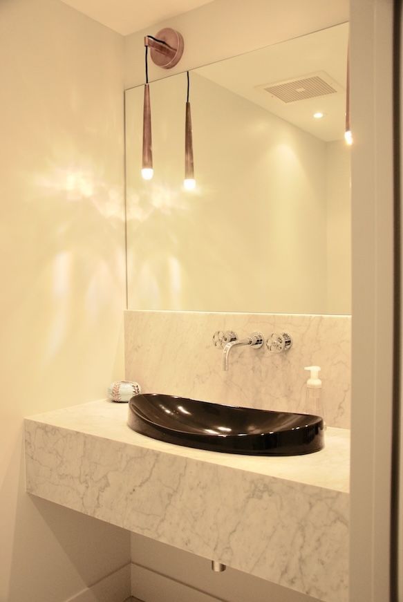 Un meuble-lavabo moderne avec un lavabo noir sur un comptoir en marbre, un grand miroir et des suspensions lumineuses.