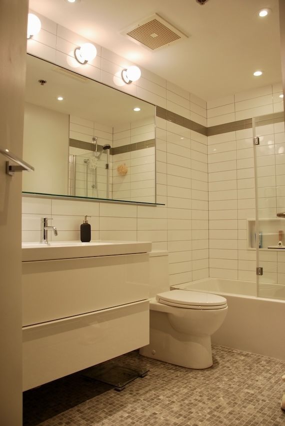 Salle de bains blanche avec meuble-lavabo suspendu, toilettes et sol en galets. Porte de douche en verre et grand miroir.