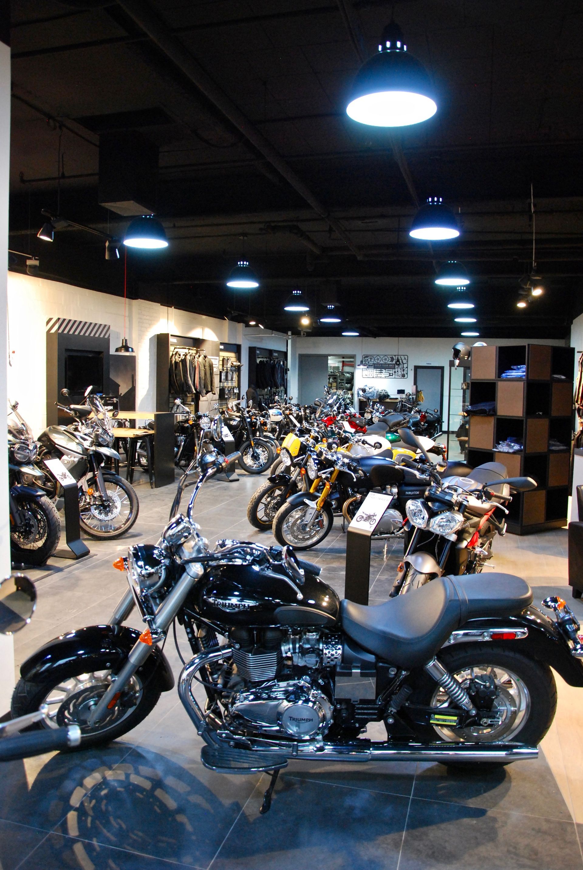 Salle d'exposition de motos présentant différents modèles, intérieur noir et blanc, éclairage zénithal.