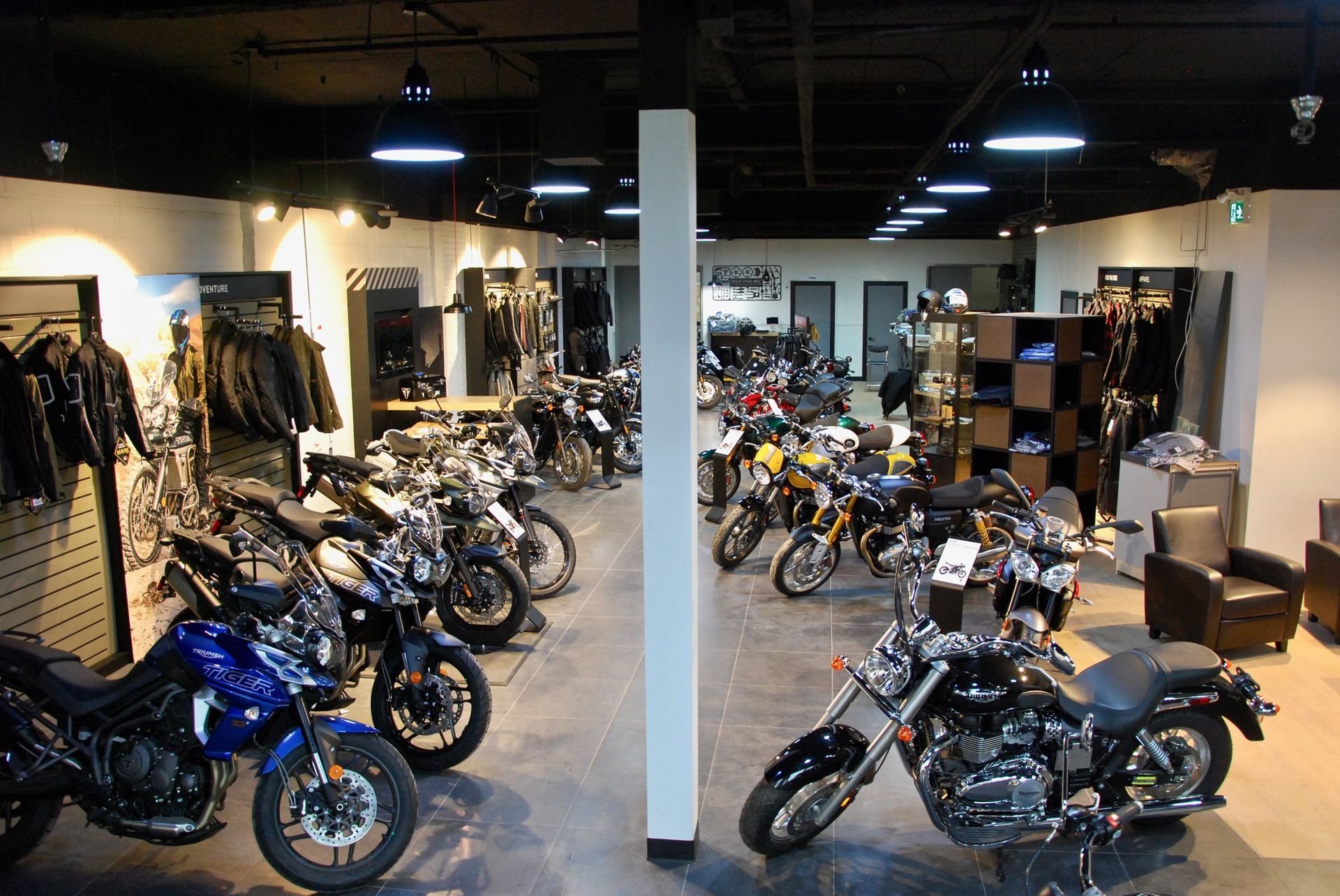Salle d'exposition de motos présentant des rangées de motos, de vêtements et d'accessoires sous un éclairage vif.