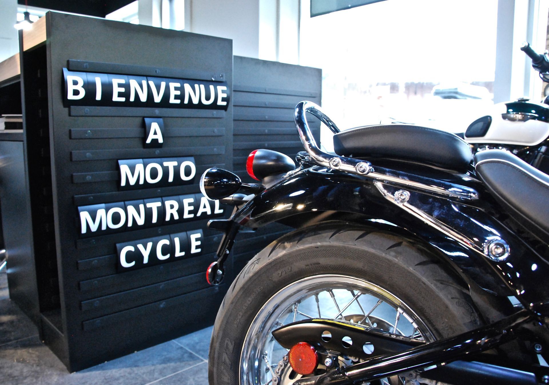 Moto noire à côté d'un panneau où l'on peut lire « Bienvenue à Moto Montréal Cycle » en lettres blanches.