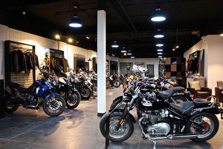 Salle d'exposition de motos avec des rangées de motos, plafond noir, blousons accrochés au mur.