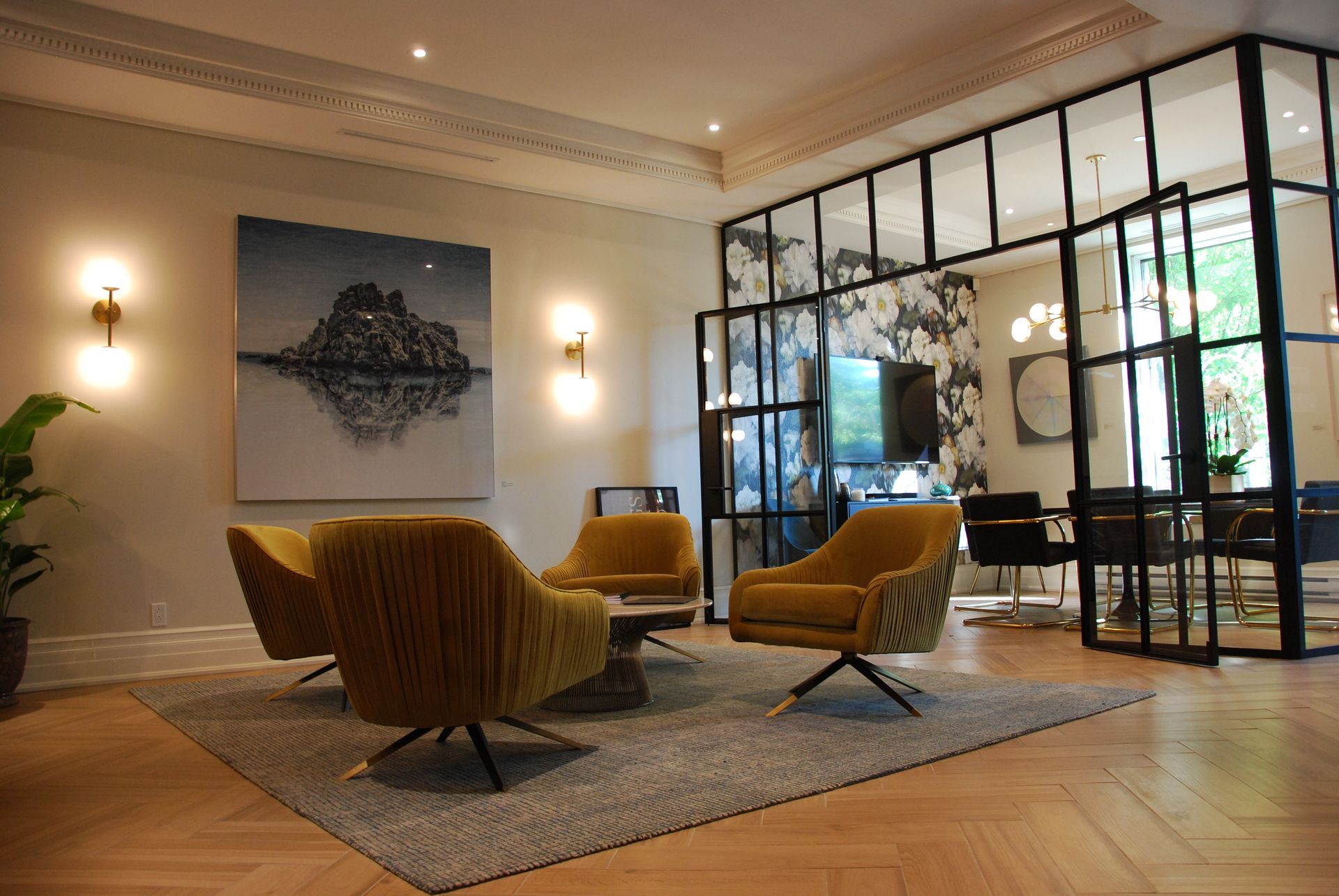 Un salon de bureau moderne avec des chaises dorées, de l'art abstrait et un espace repas aux parois de verre.
