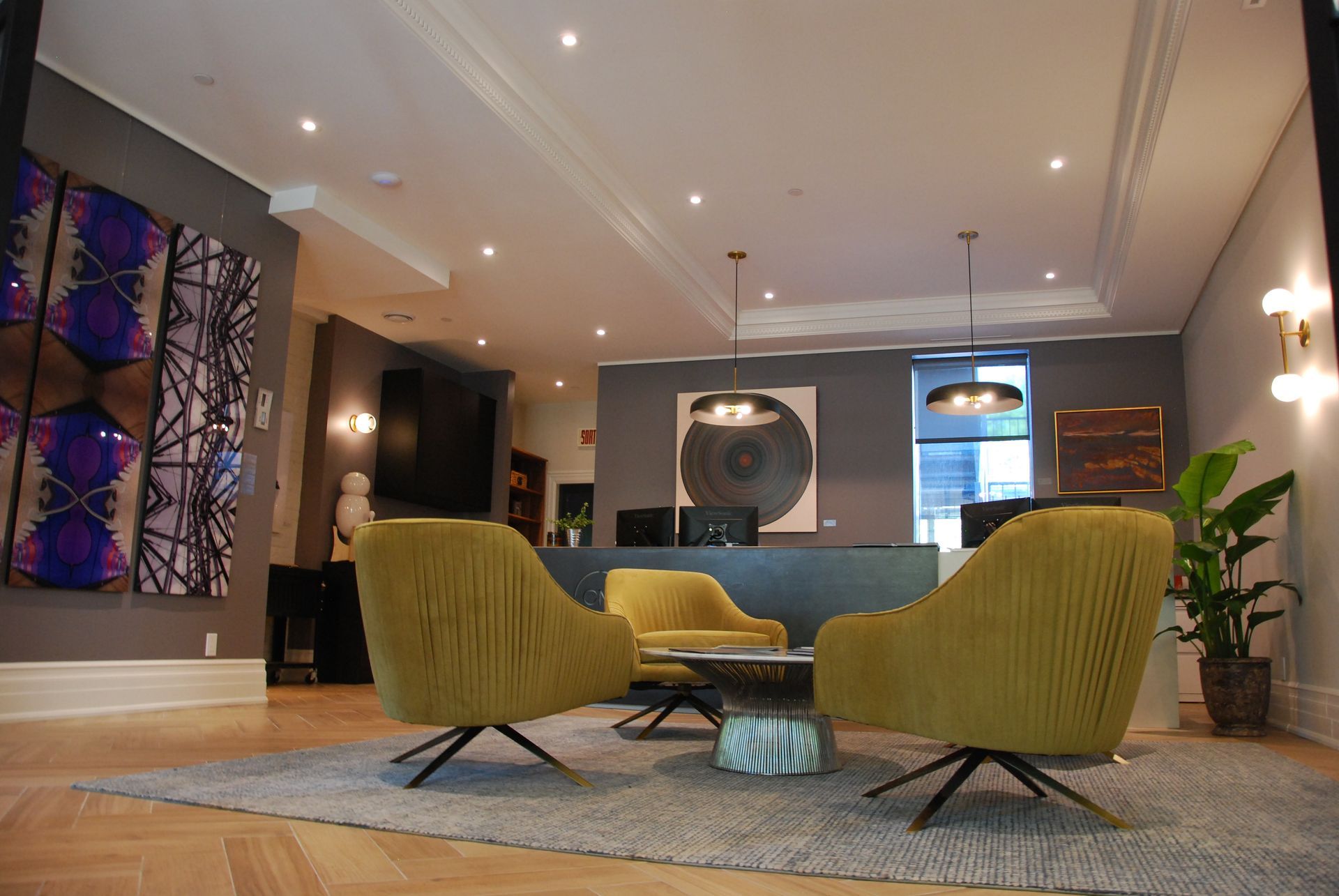Coin détente avec trois fauteuils jaunes, des œuvres d'art, des murs gris et un tapis.