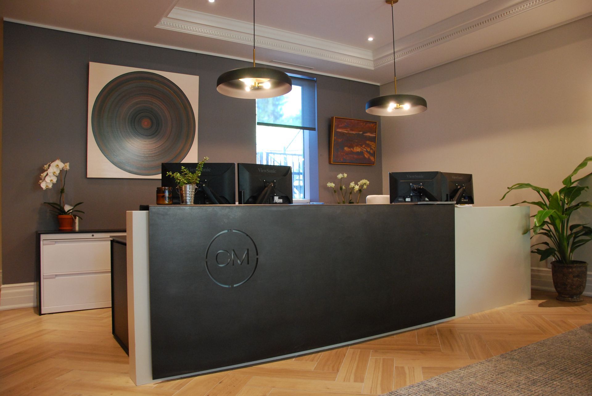 Bureau d'accueil moderne avec œuvres d'art, plantes et écrans d'ordinateur.