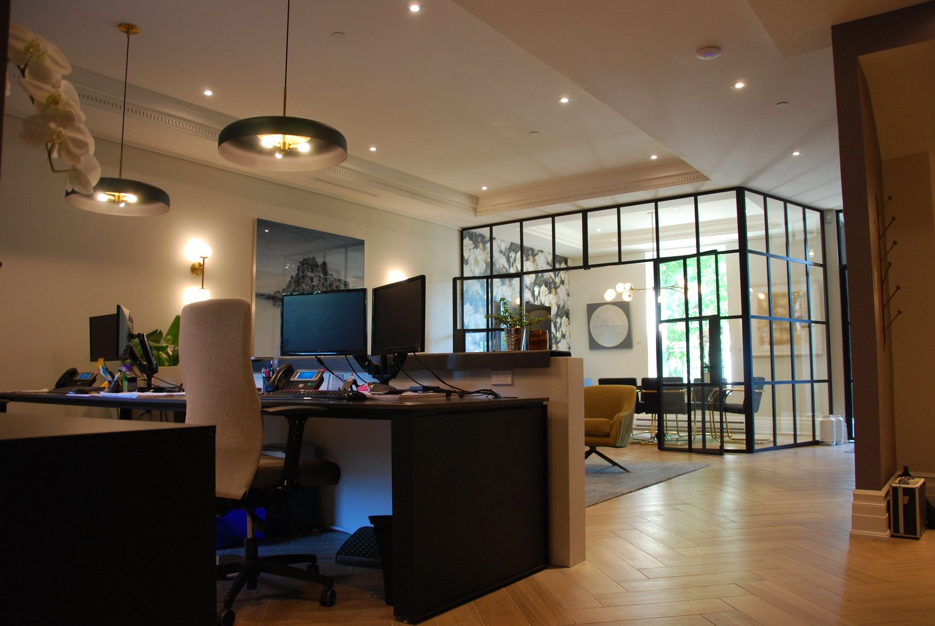 Espace de bureaux moderne avec bureaux, pièce aux parois vitrées et luminaires suspendus.