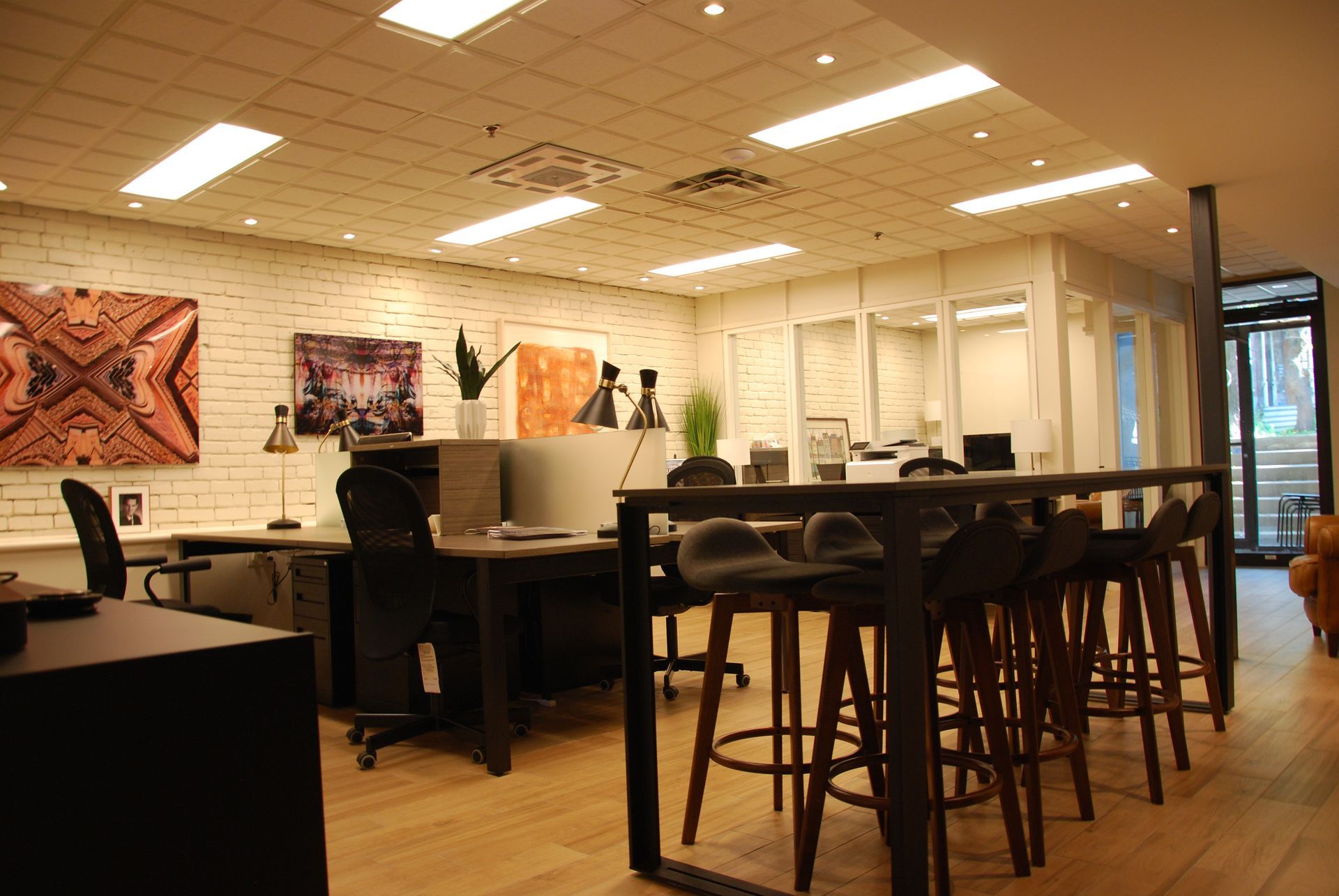 Espace de bureau moderne avec bureaux, table haute, œuvres d'art et grandes fenêtres.