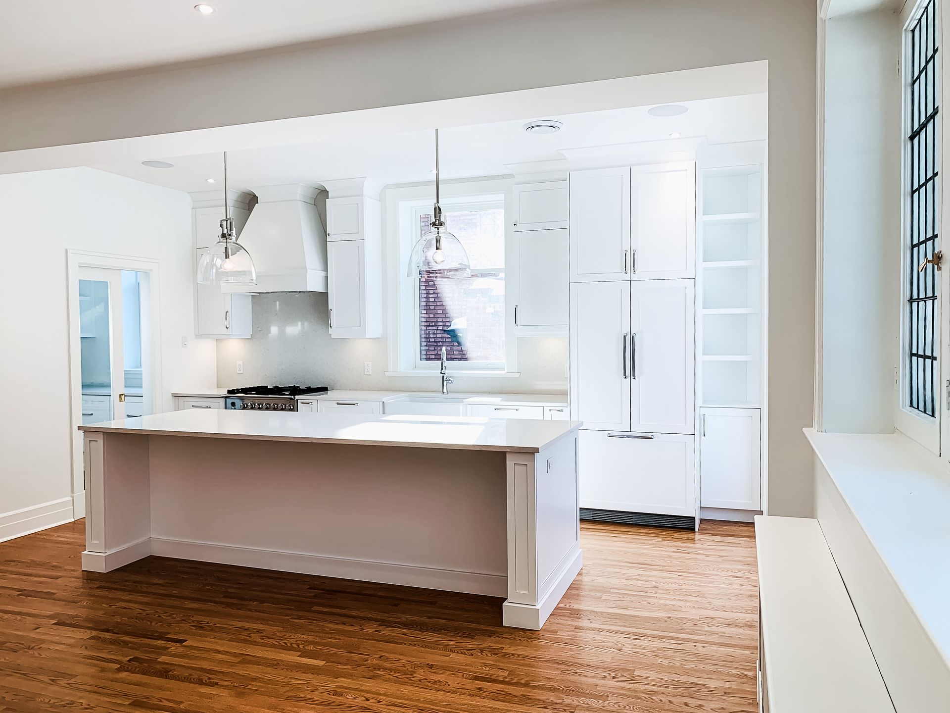 Cuisine blanche lumineuse avec îlot central, placards et électroménager. Parquet et lumière naturelle.