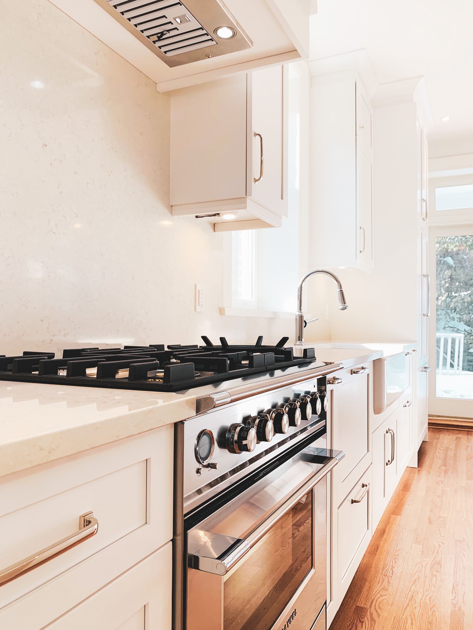 Cuisine blanche lumineuse avec four, plaque de cuisson et évier en acier inoxydable. Sol, placards et hotte en bois.