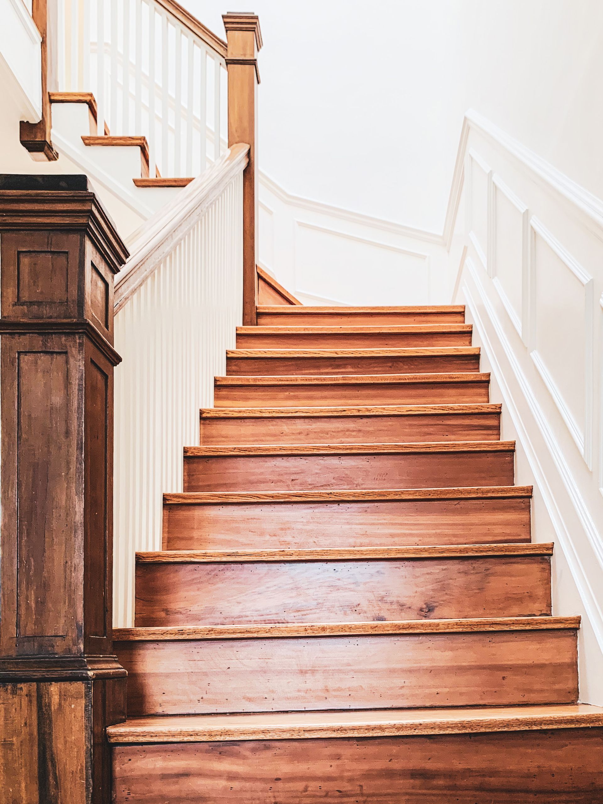 Escalier en bois avec rampe blanche contre un mur blanc.