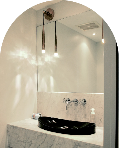 Salle de bains avec lavabo noir, comptoir en marbre, grand miroir et luminaires suspendus.