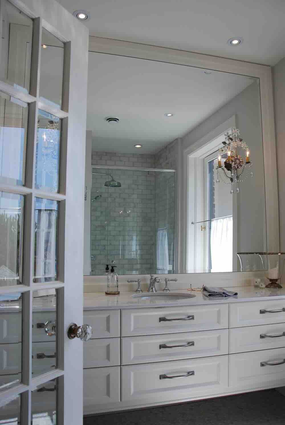 Salle de bains avec grand miroir au-dessus d'un meuble-lavabo blanc et douche en verre.
