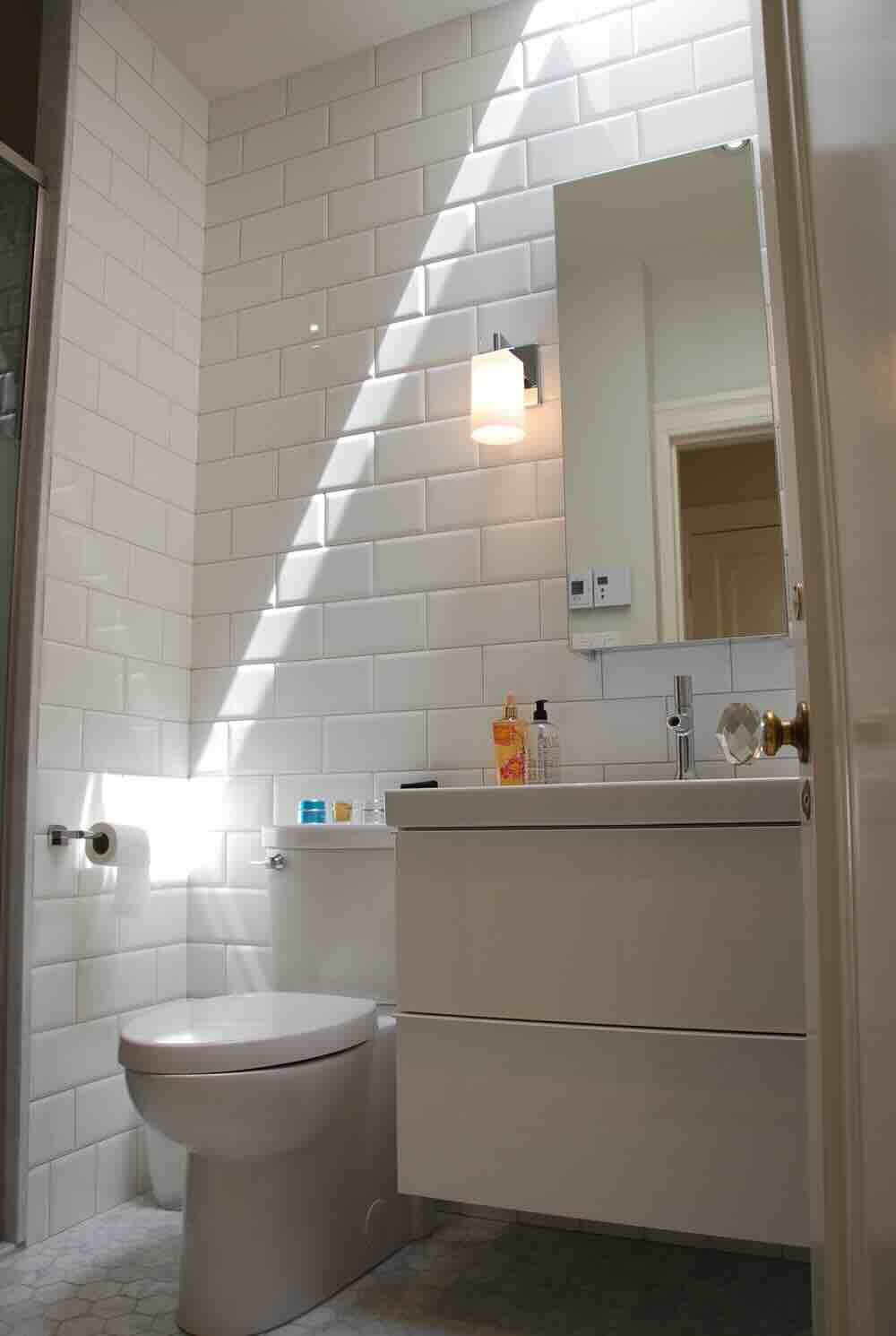 Petite salle de bains blanche avec toilettes, lavabo et murs carrelés, baignée de lumière naturelle grâce à un puits de lumière.