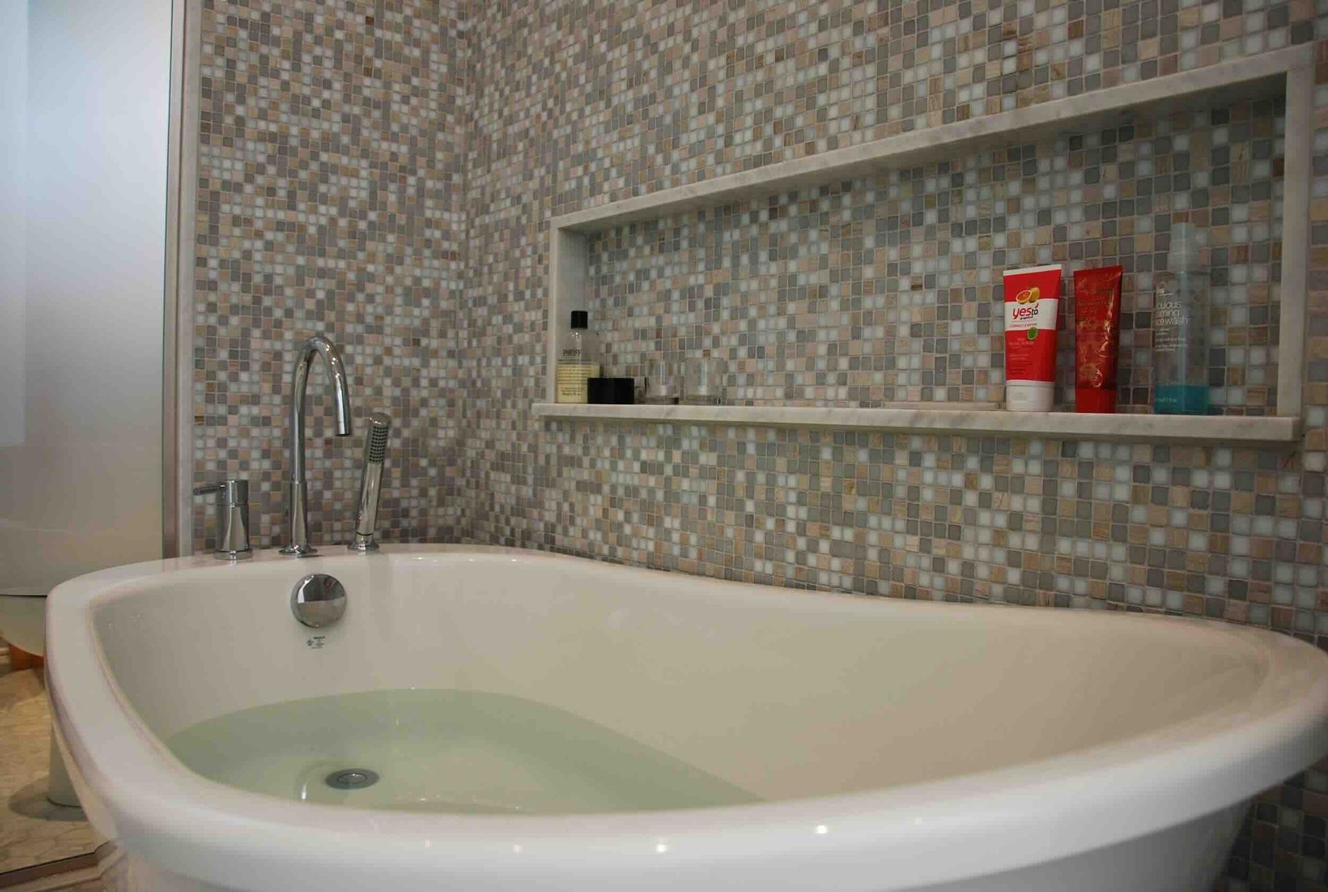 Baignoire blanche remplie d'eau ; murs carrelés avec étagère intégrée contenant les articles de toilette.