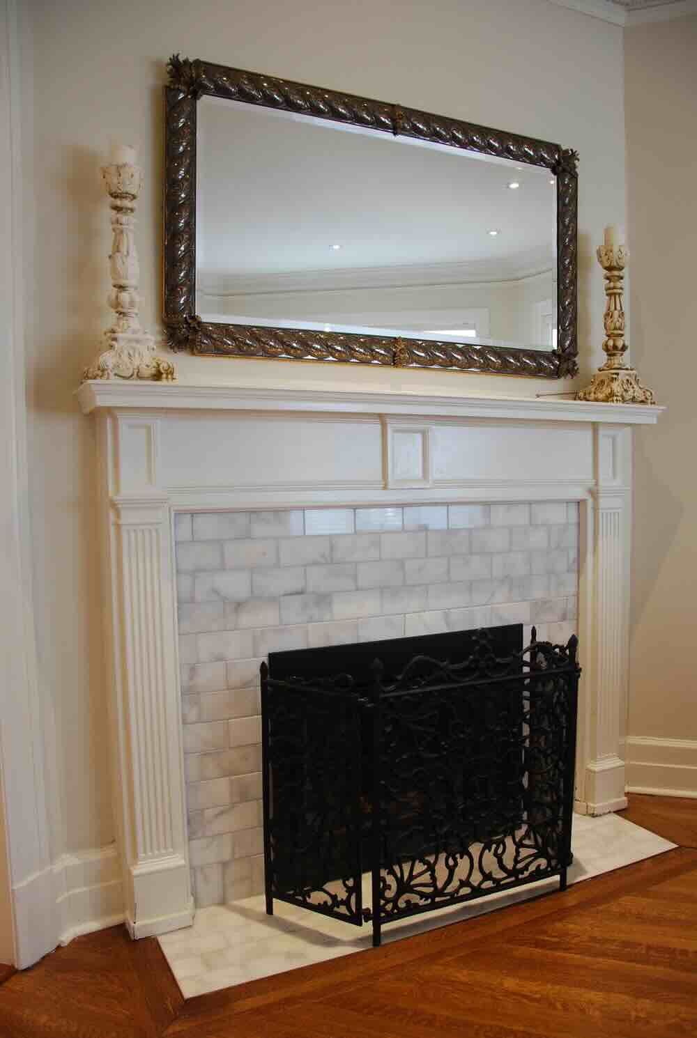 Cheminée blanche avec carrelage en marbre, paravent noir, grand miroir et bougeoirs décoratifs.