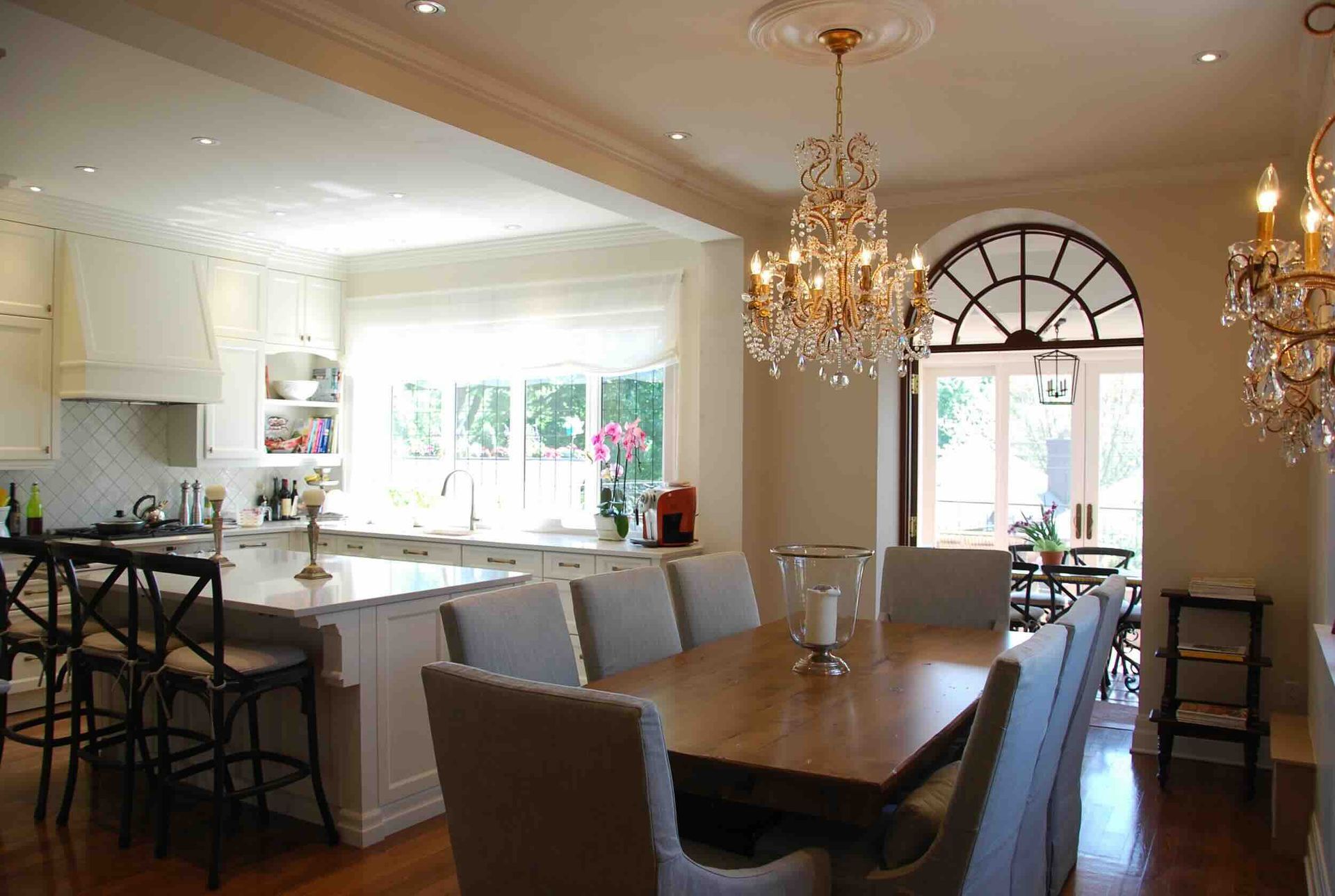 Cuisine et salle à manger ouvertes avec lustre, grandes fenêtres et table dressée pour un repas.
