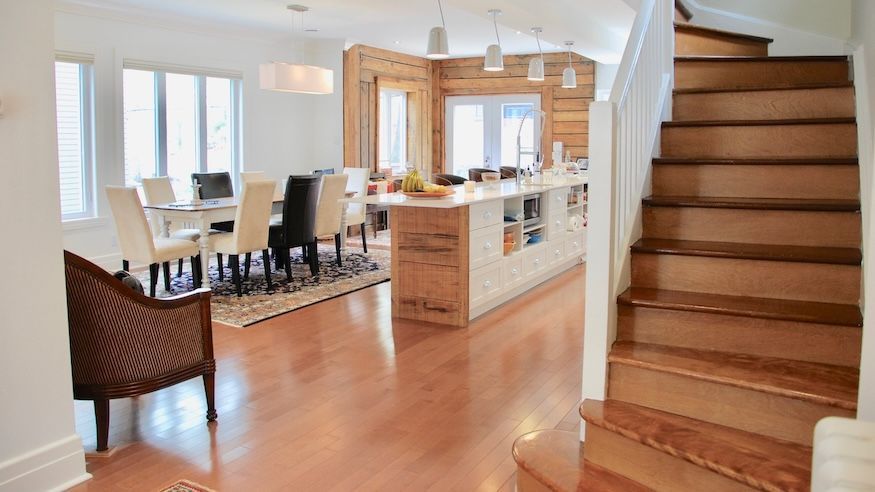 Un escalier en bois mène à une maison moderne comprenant un coin repas, un îlot de cuisine et un parquet.