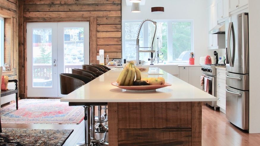 Cuisine rustique avec des touches de bois et de blanc, îlot avec sièges, appareils électroménagers en acier inoxydable, fruits.