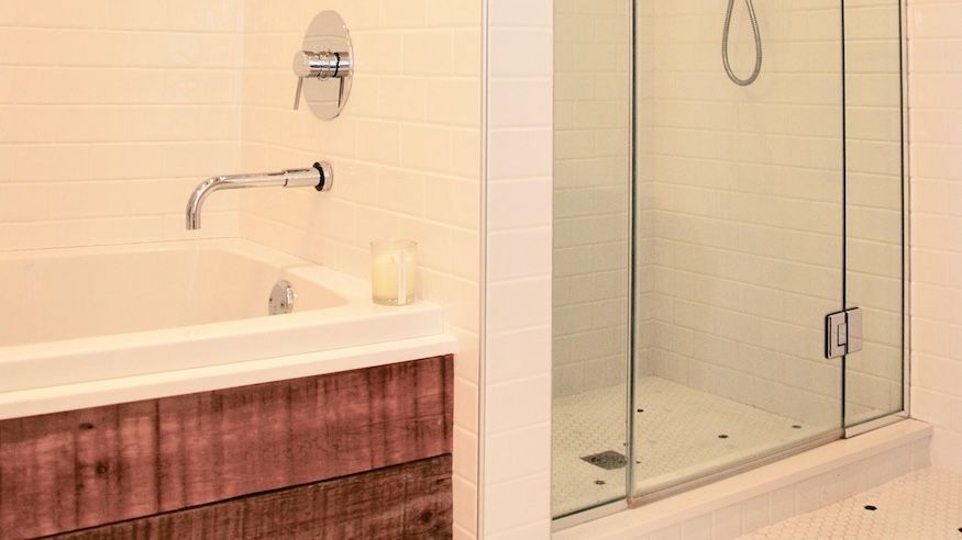 Salle de bains avec baignoire blanche, douche en verre et meuble-lavabo en bois.