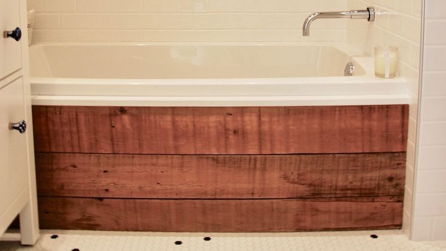 Baignoire avec panneaux de bois rustiques sur la façade. Baignoire blanche et murs carrelés.