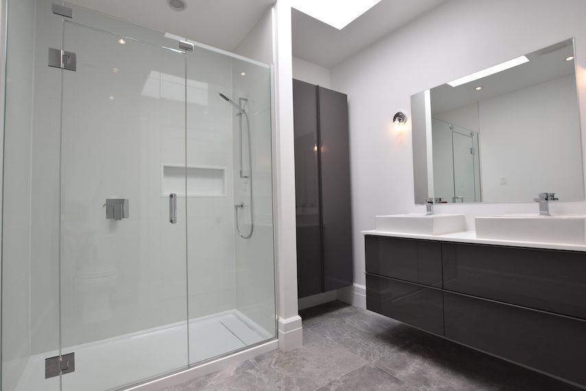 Salle de bains moderne avec grande douche en verre, meuble-lavabo gris foncé et armoire de rangement haute.
