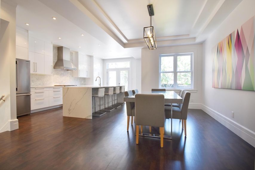 Cuisine et salle à manger modernes avec îlot en marbre, appareils électroménagers en acier inoxydable, parquet foncé et grande fenêtre.