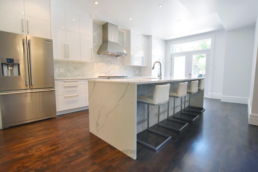 Cuisine moderne blanche avec électroménagers en acier inoxydable, grand îlot avec sièges et plancher en bois foncé.