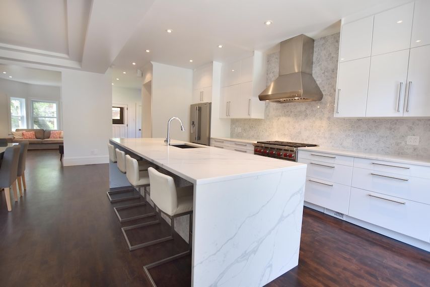 Cuisine moderne blanche avec îlot central, appareils électroménagers en acier inoxydable et parquet foncé.