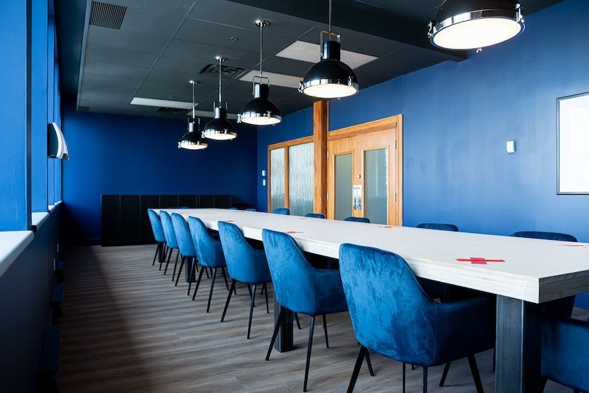 Salle de conférence avec murs bleus, longue table blanche, chaises bleues et luminaires suspendus.