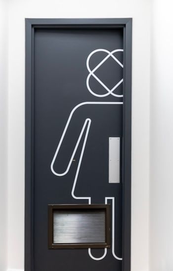 Porte sombre avec un symbole de toilettes en contour blanc et une petite fenêtre.