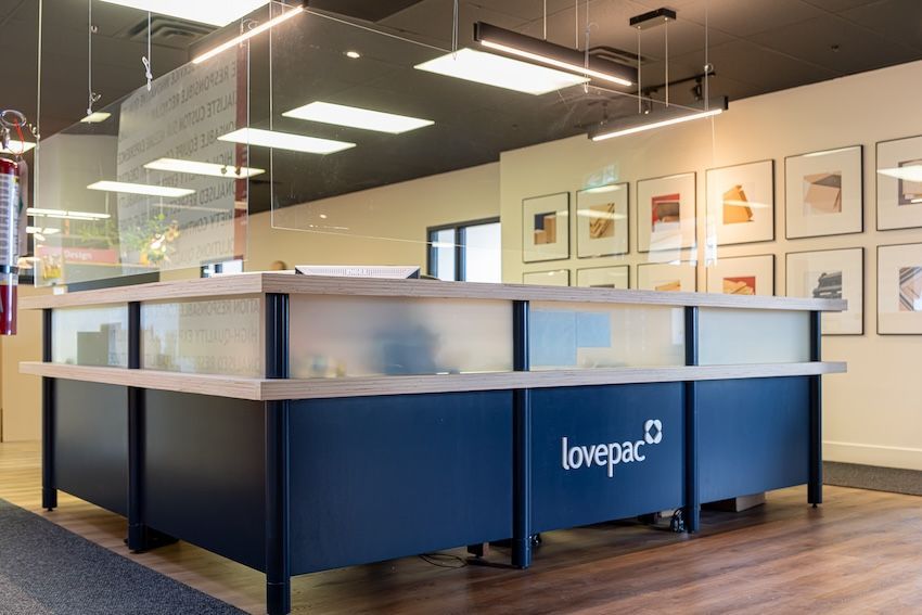Comptoir d'accueil orné du logo « lovepac », base bleu marine, garnitures en bois, verre dépoli et œuvre d'art encadrée au mur.