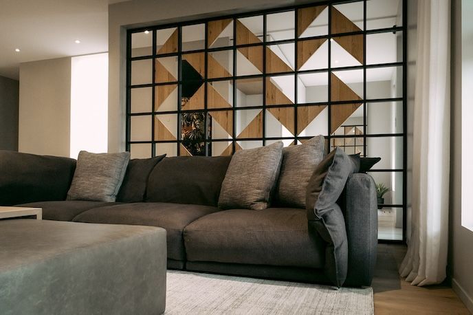 Canapé gris dans un salon, avec des panneaux muraux géométriques en bois et en miroir derrière.