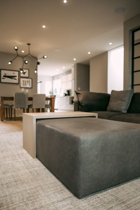 Salon moderne avec canapé d'angle gris foncé, pouf et table à manger.