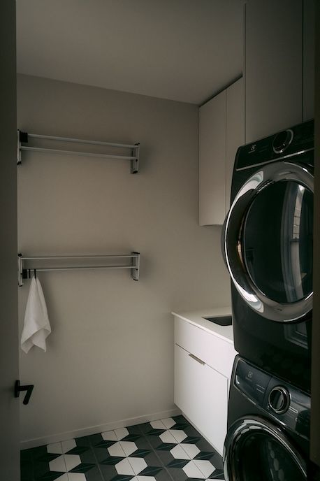 Buanderie avec lave-linge et sèche-linge noirs superposés, placards blancs et sol à motifs.