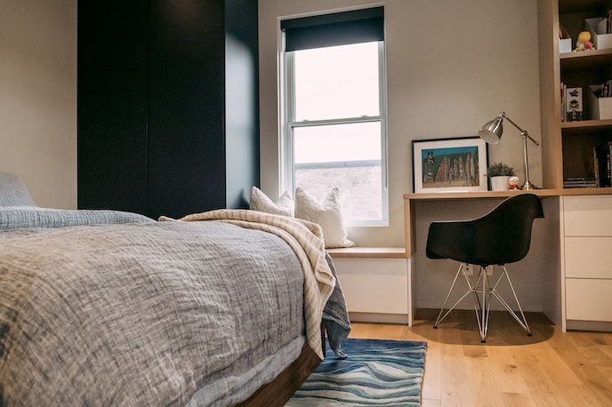 Chambre avec lit, bureau, chaise noire, fenêtre, étagères intégrées et placard sombre.