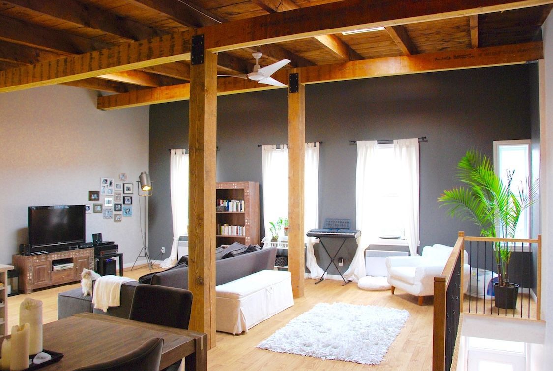 Intérieur de loft spacieux avec poutres en bois apparentes, murs, meubles et fenêtres gris et blancs.
