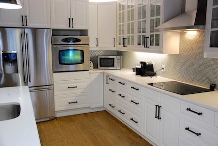 Cuisine blanche avec appareils électroménagers en acier inoxydable, armoires blanches et parquet clair.